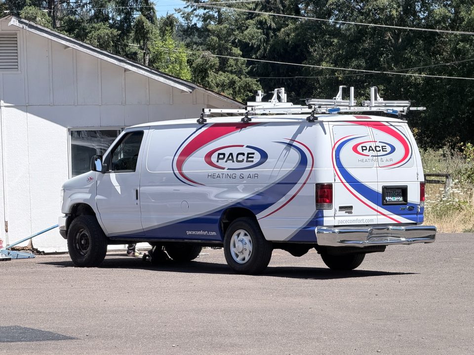 A Pace Heating & Air service van wrapped in the blue and red company logo, parked outside the Albany, Oregon shop with the CCB license number on the door